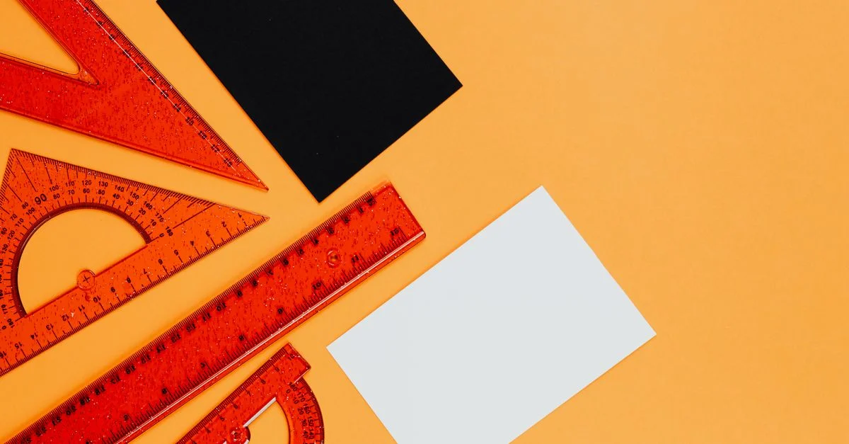 Règles orange vibrantes et outils géométriques sur un fond orange avec des cartes noires et blanches.