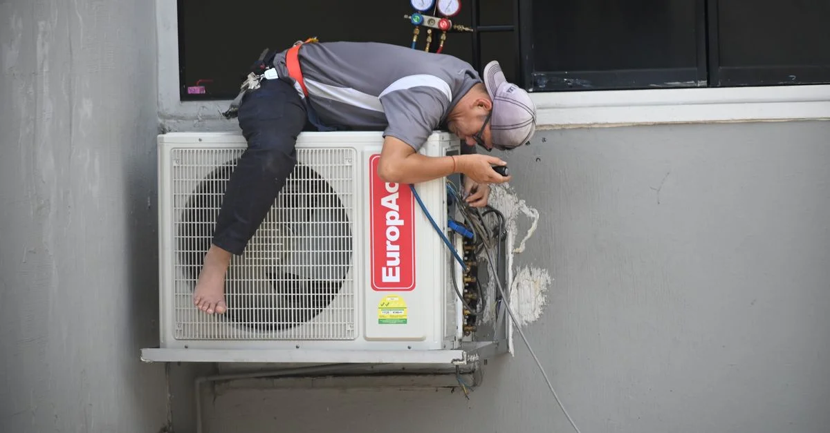 Un technicien répare habilement une unité de climatisation extérieure montée sur un mur de bâtiment.