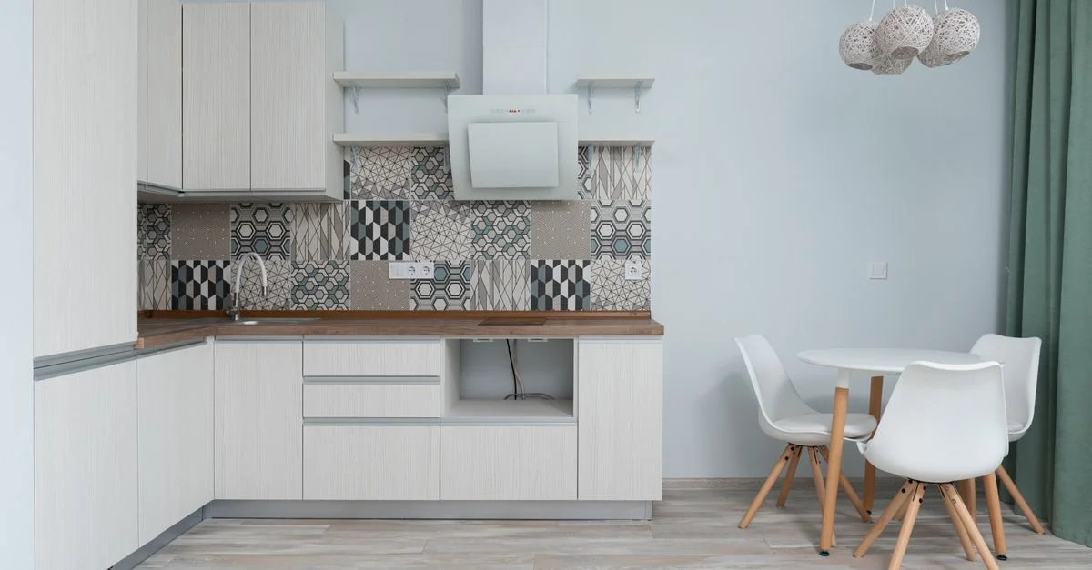 Un intérieur de cuisine moderne et minimaliste avec des armoires blanches élégantes et un dosseret en carrelage géométrique.