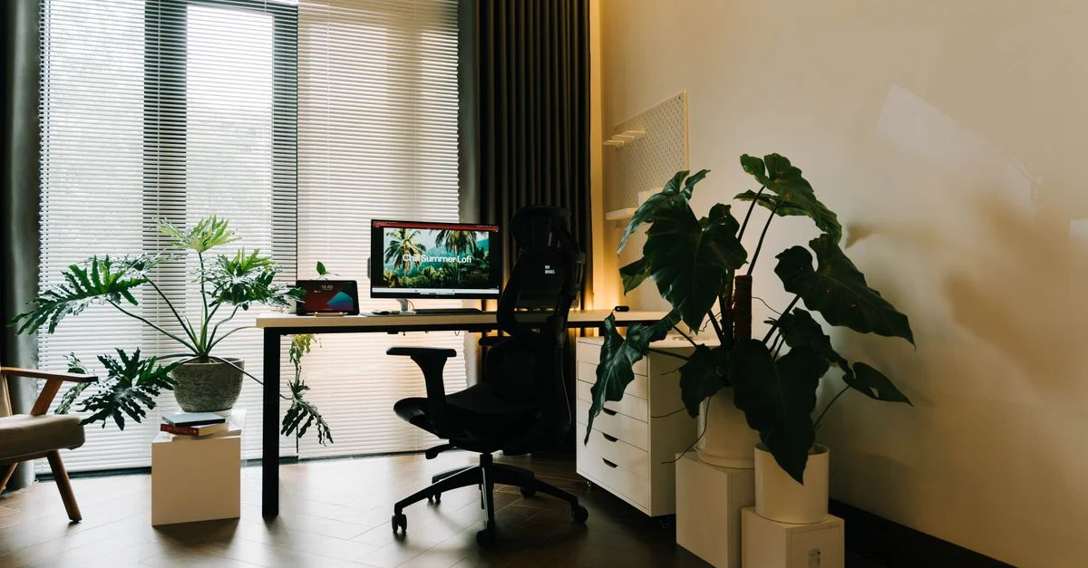 Un bureau à domicile élégant avec de grandes fenêtres, un bureau avec un ordinateur et des plantes d'intérieur luxuriantes.